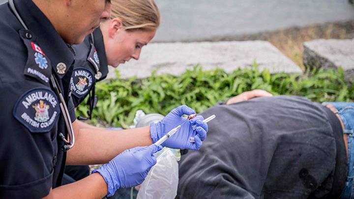 paramedics administering naloxone to patient laying on the ground